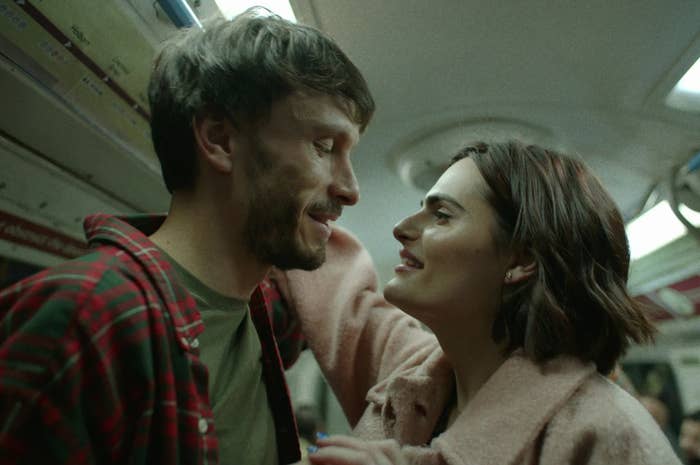 Two actors in a tender moment on a subway, with one touching the other’s face, expressing affection