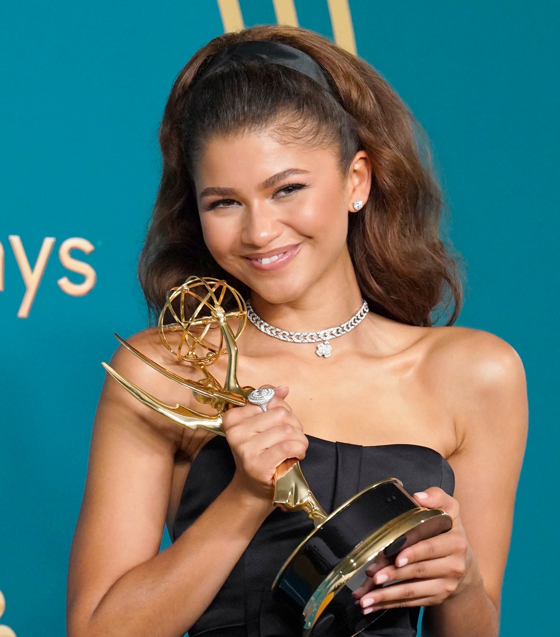 Zendaya in a strapless gown holding an Emmy award. She wears a silver necklace and has her hair in an updo
