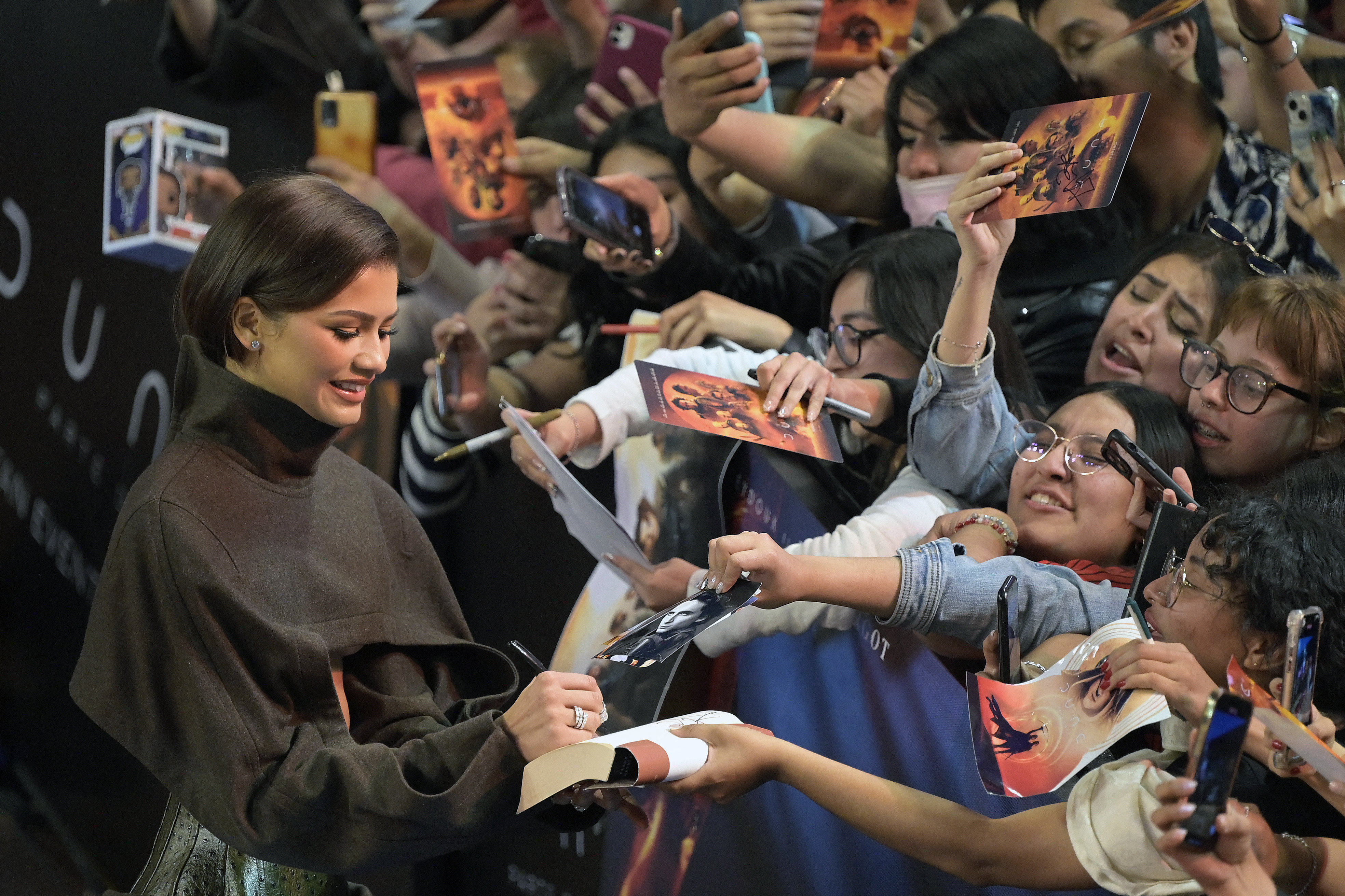 Zendaya interacting with fans and signing autographs while wearing a casual sweater