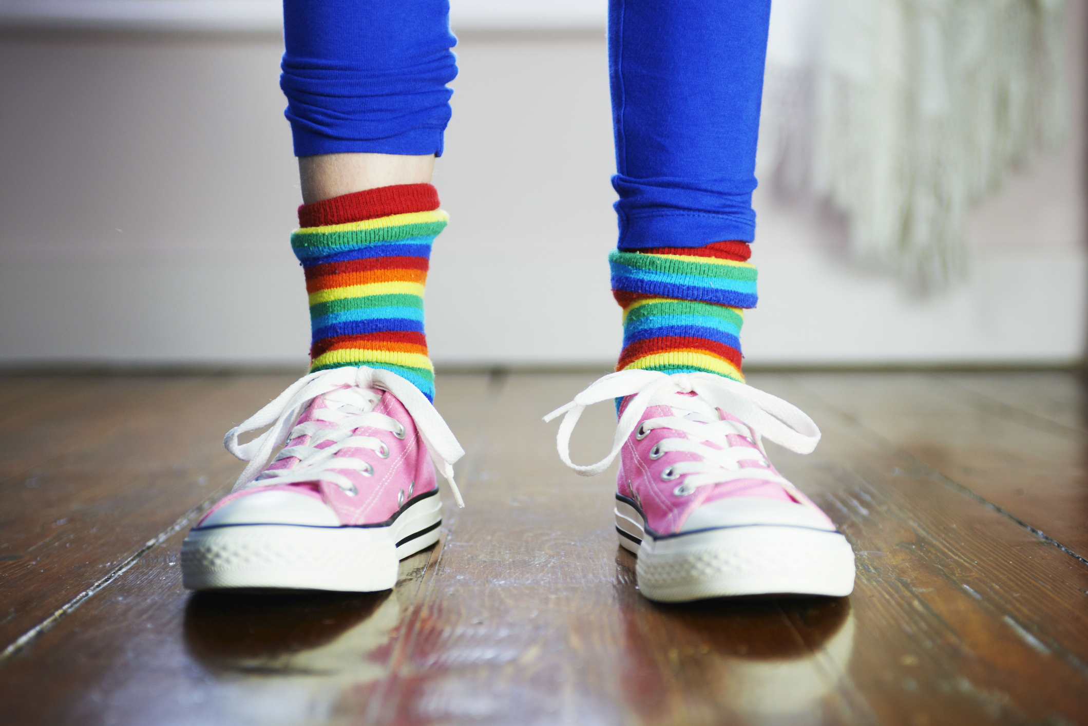 kid wearing pink sneakers and rainbow-striped socks standing on a wooden floor