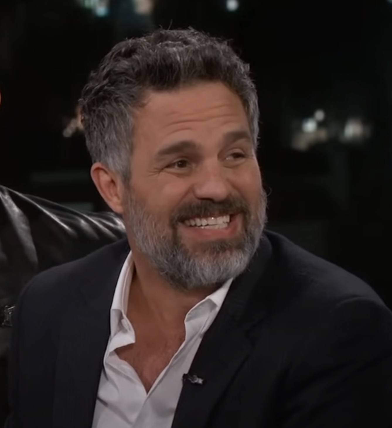 Mark Ruffalo in a suit, white shirt, no tie, smiling in an interview setting