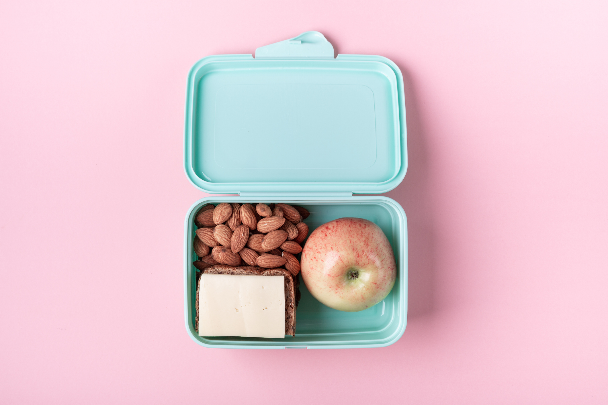 Lunchbox with almonds, an apple, and a sandwich on a pink background