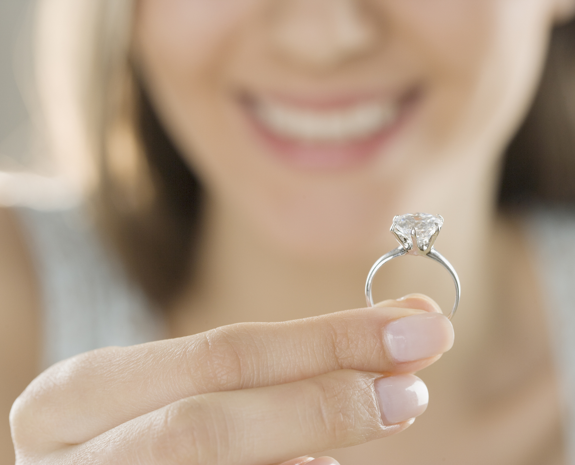 Close-up of a person holding a diamond ring, focusing on the ring with a smiling face in the background