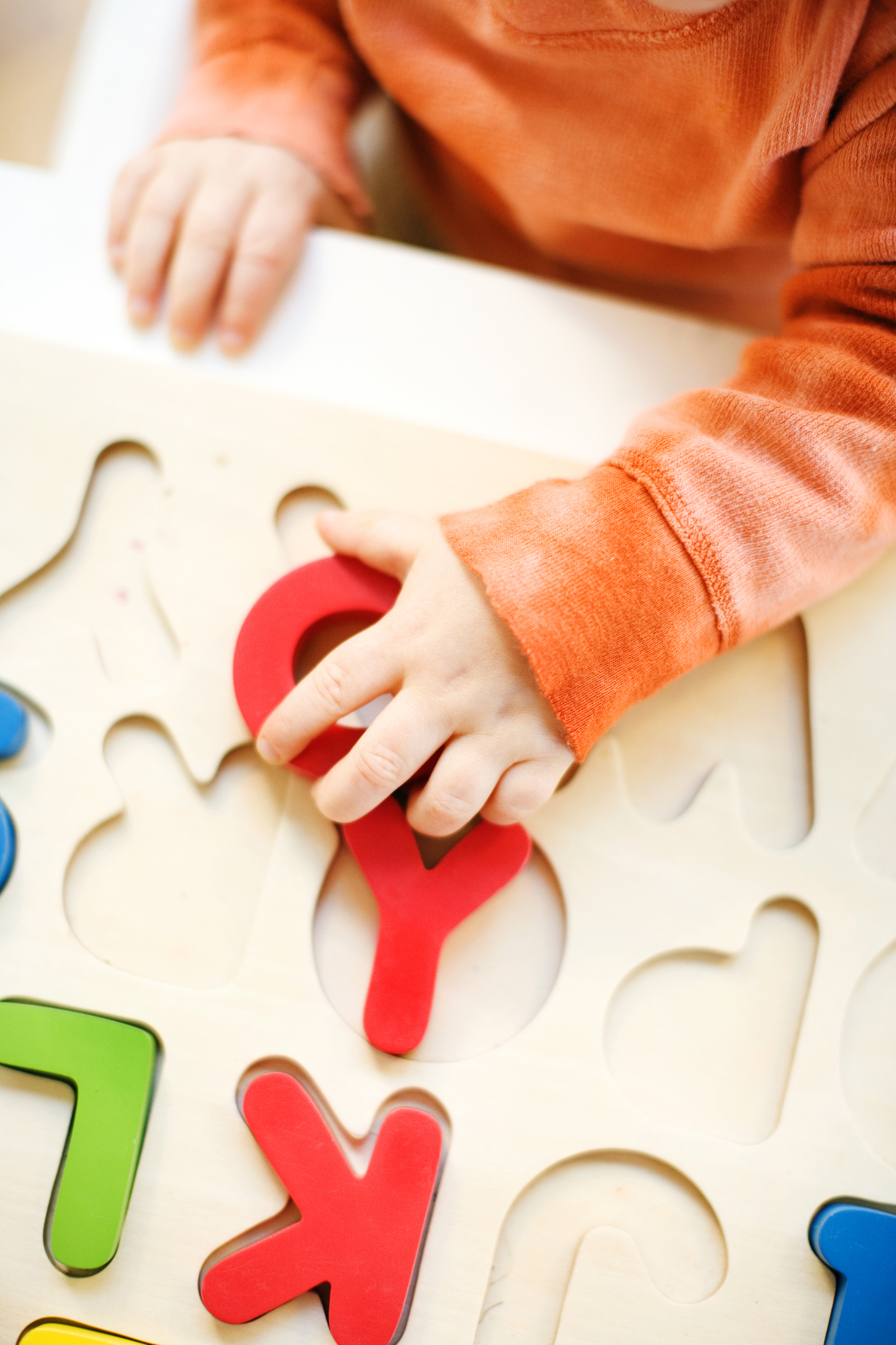 Child&#x27;s hand solving a wooden puzzle, placing a red piece