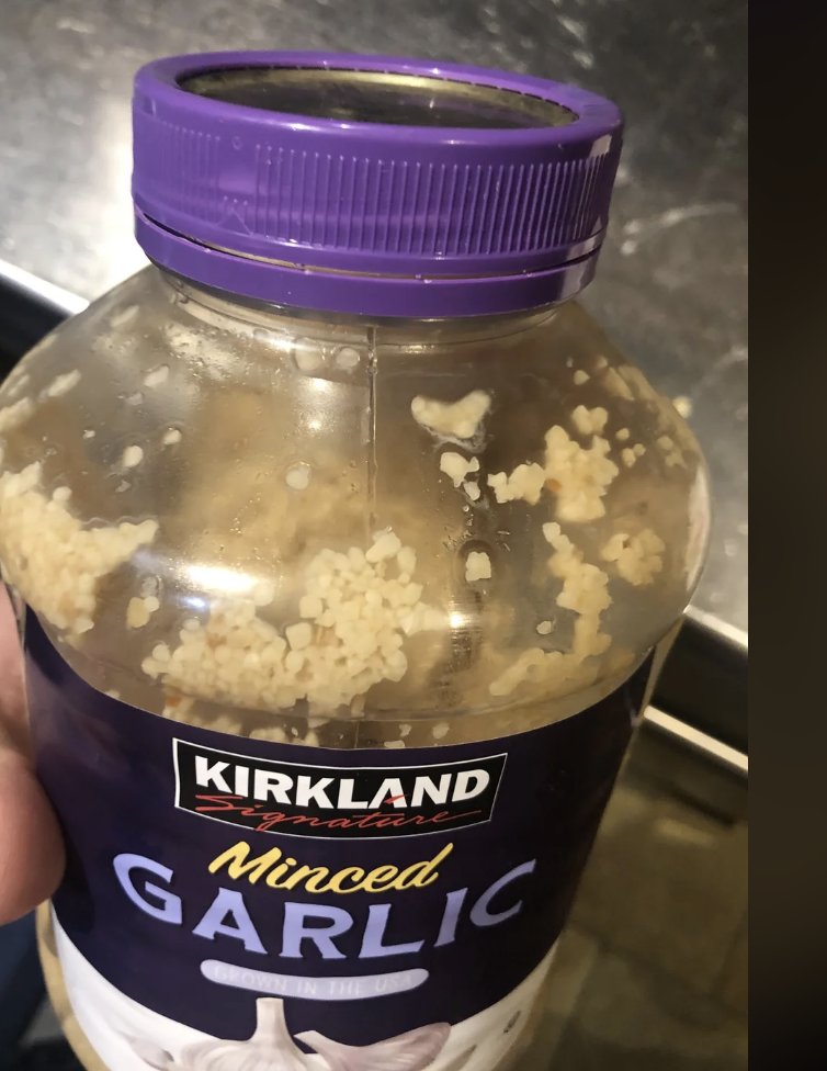 Person holding a Kirkland minced garlic jar with garlic pieces stuck to the lid