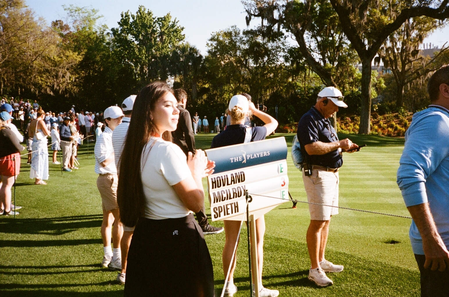 Person holding sign with golfer names Hovland and Spieth at a golf event, with spectators in the background