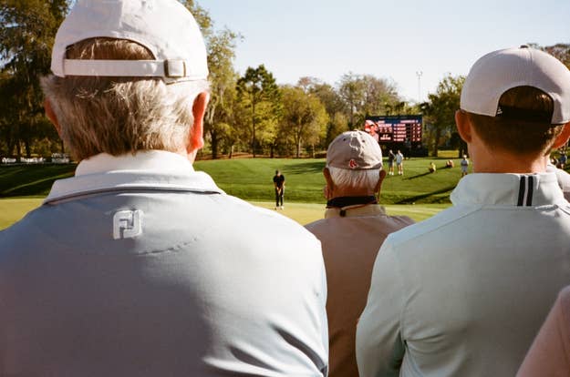 Three spectators watching a golf tournament, with a golfer in the distance preparing to swing