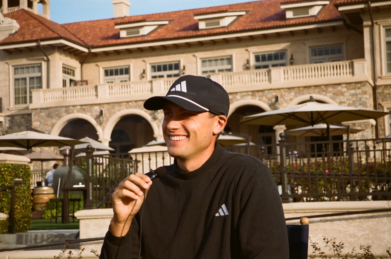 Man in adidas cap and sportswear smiling outside a clubhouse