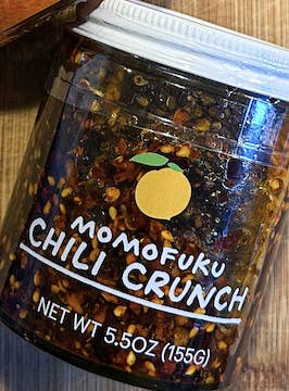 A jar of Momofuku Chili Crunch on a wooden surface
