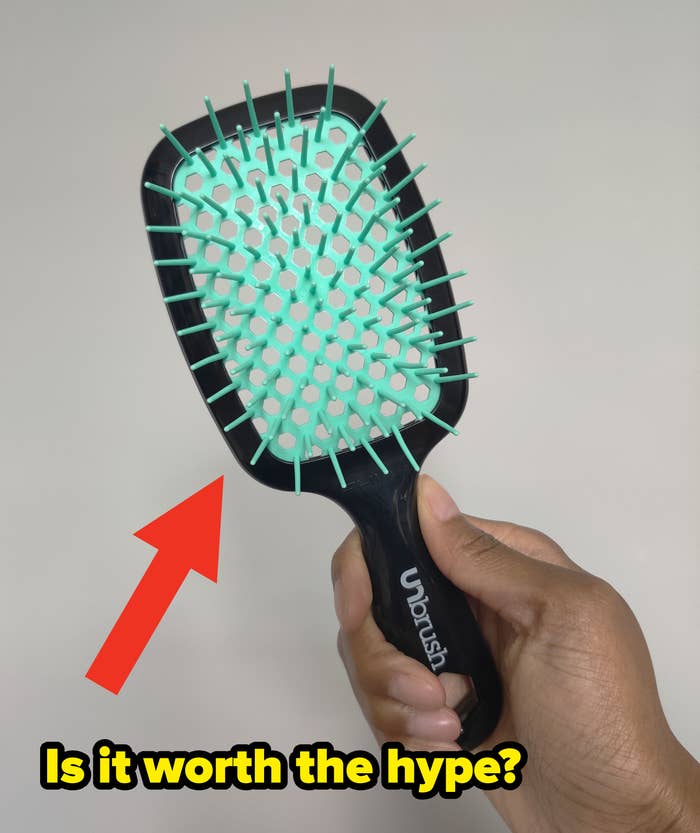 Person holding a black hairbrush with aqua bristles against a neutral background