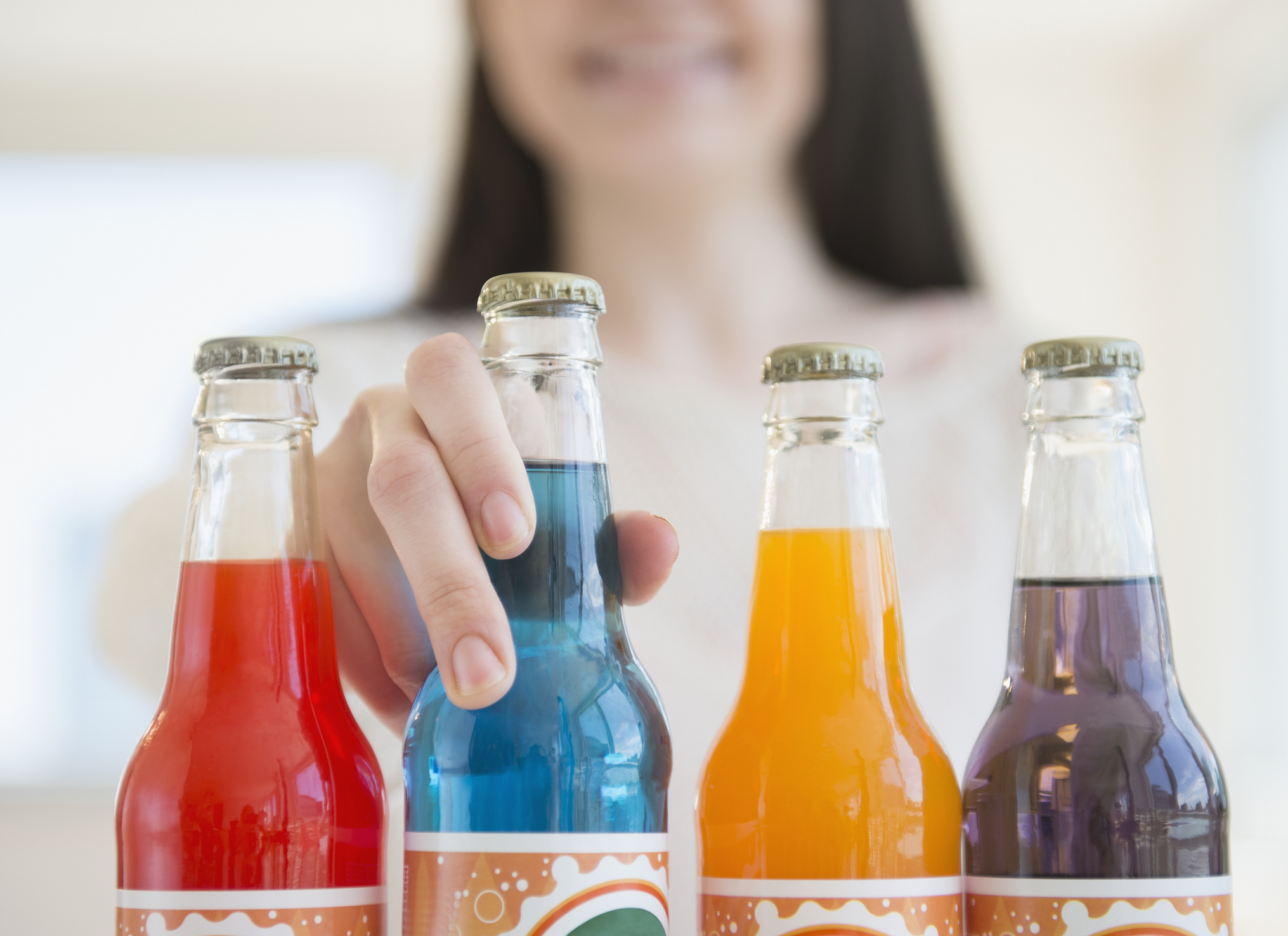 Person selecting one of four colorful soda bottles. Article context: Food