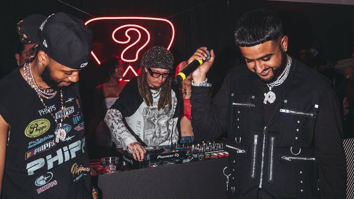 Three DJs at a mixing console at a club event, focused on music equipment