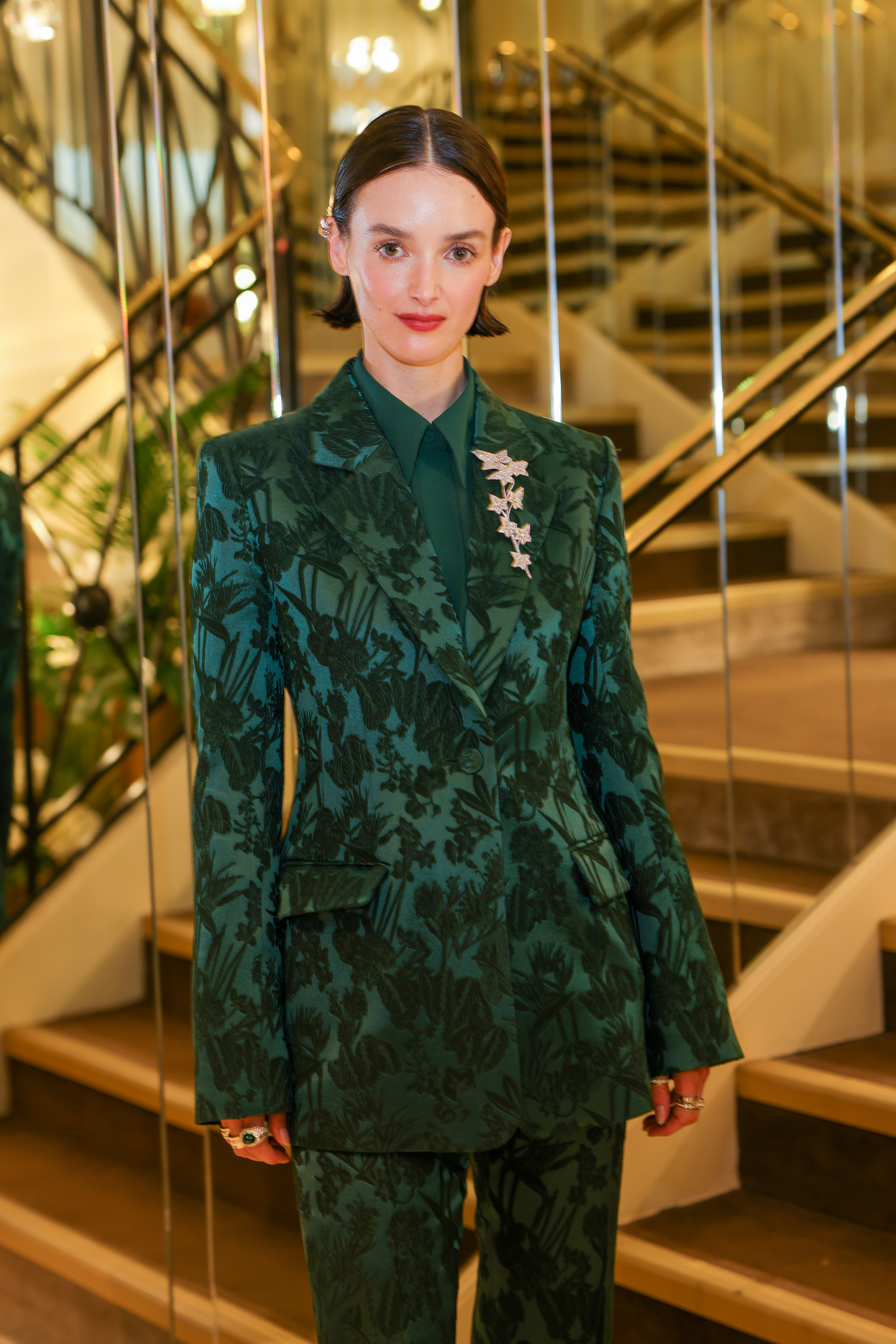 Woman in patterned green suit stands on staircase at event