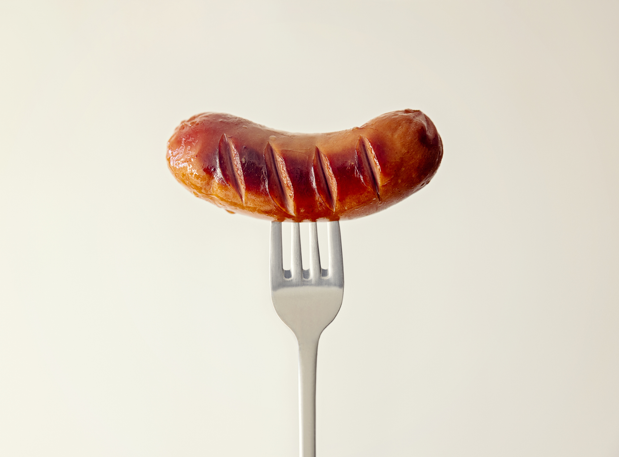 Grilled sausage skewered on a fork against a plain background