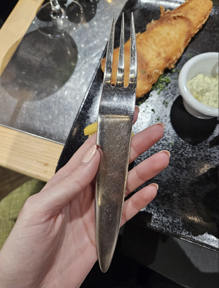 Person holding a utensil with fork tines at one end and a knife edge at the other, over a plate of food