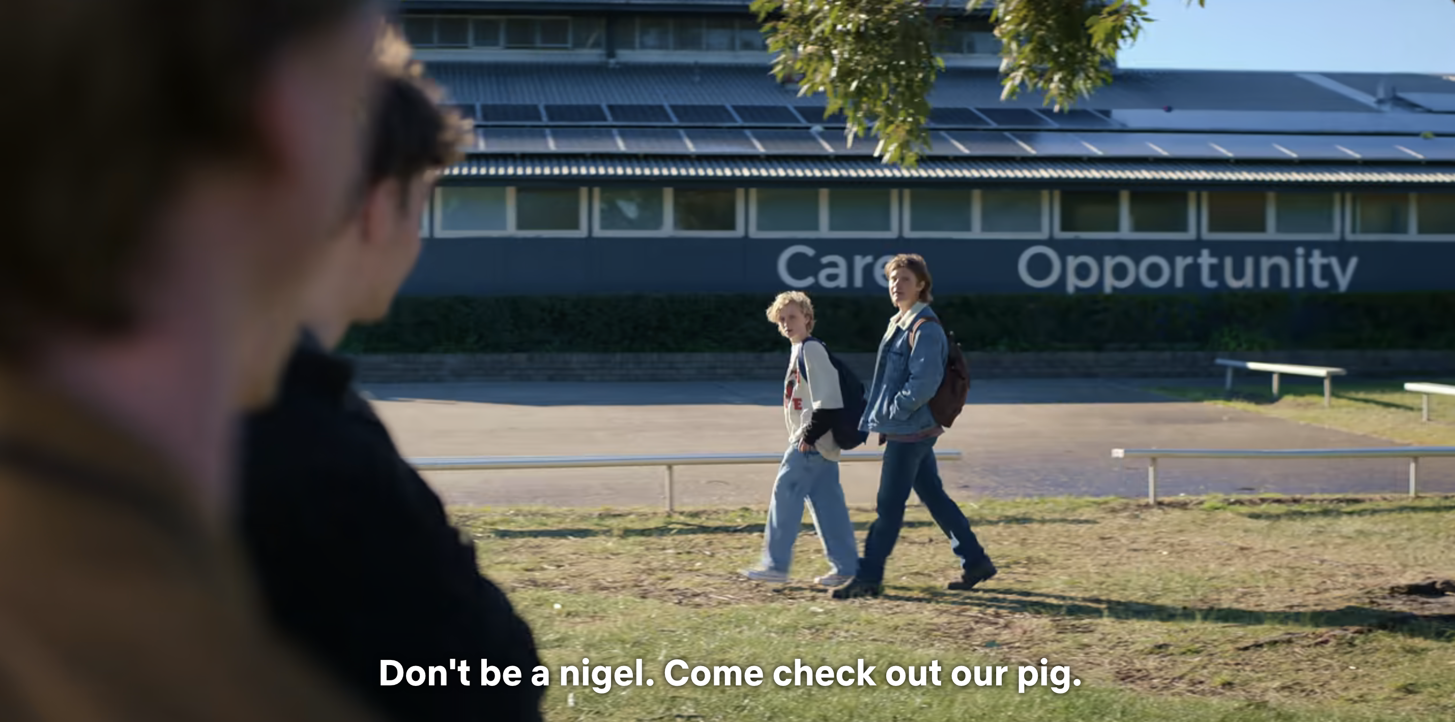 Two actors from a TV show walk and talk outside a school with captions displaying dialogue