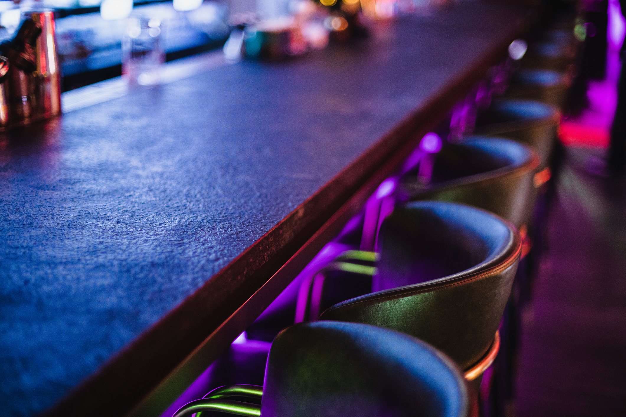 Empty bar counter with stools in a dimly lit setting, suggestive of a quiet nightlife scene