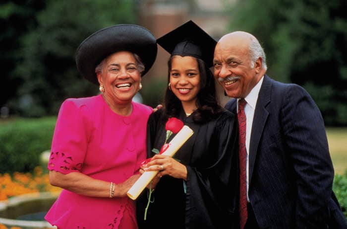 Graduate smiling with her supportive parents, each side by side, holding a diploma, on graduation day