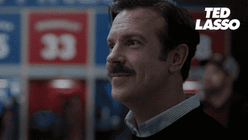 Ted Lasso character smiling in a sports stadium setting