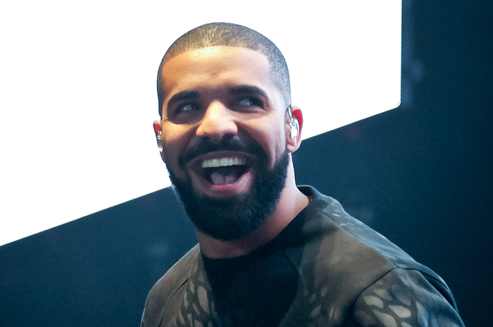 Drake smiling on stage with a microphone, wearing a patterned shirt