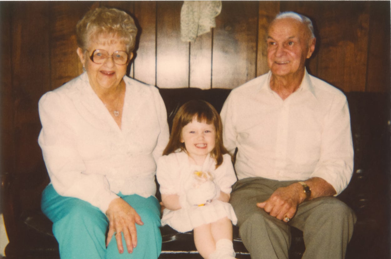 Elderly couple seated with young girl smiling between them indoors