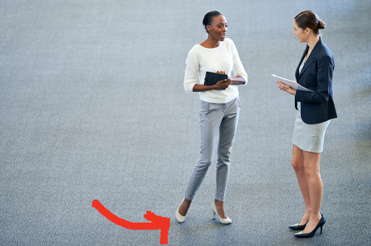 Two professionals engaging in conversation, one holding a tablet. Arrow points to the one standing with one foot raised
