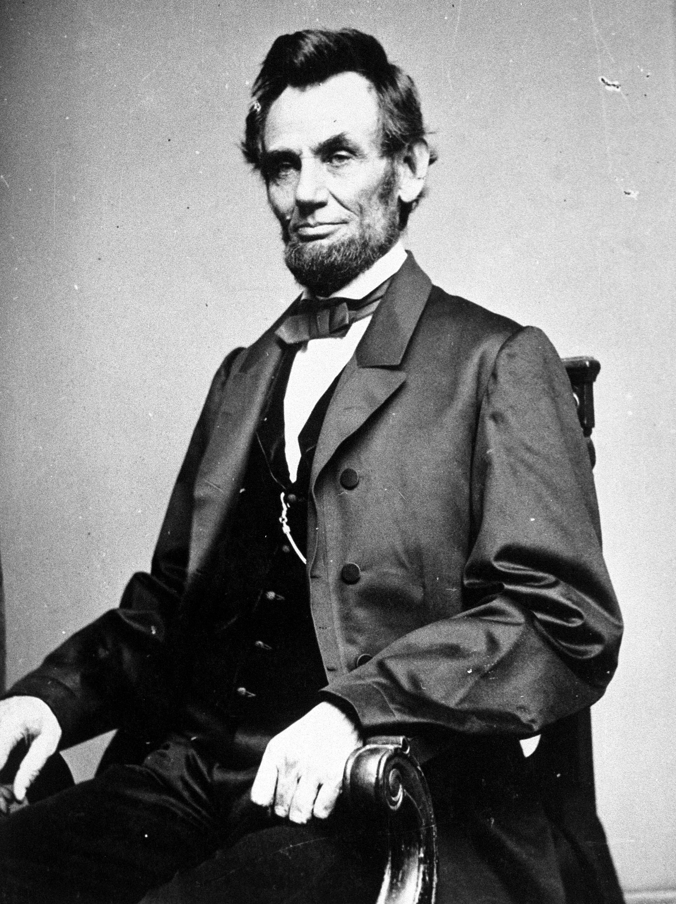 Portrait of Abraham Lincoln seated in a chair with a bow tie and formal coat