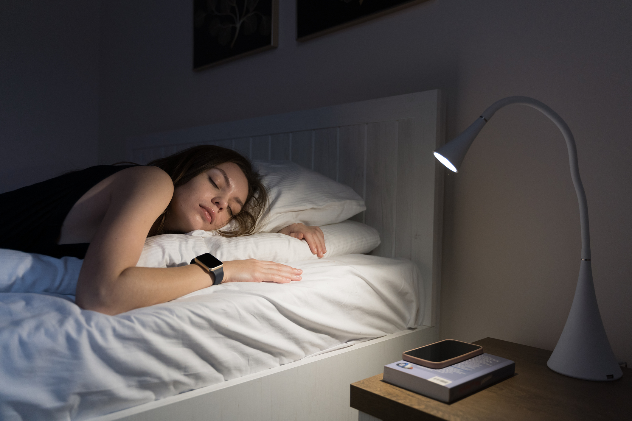 Woman sleeping in bed with a book and illuminated bedside lamp