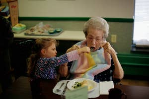 Young girl helps elderly woman eat, both sitting at a table, reflecting family care