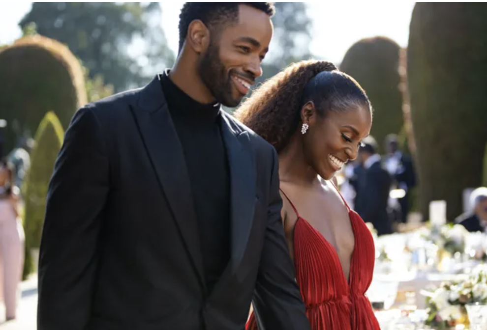 Couple in formal attire smiling together, man in a black suit and woman in a pleated red dress