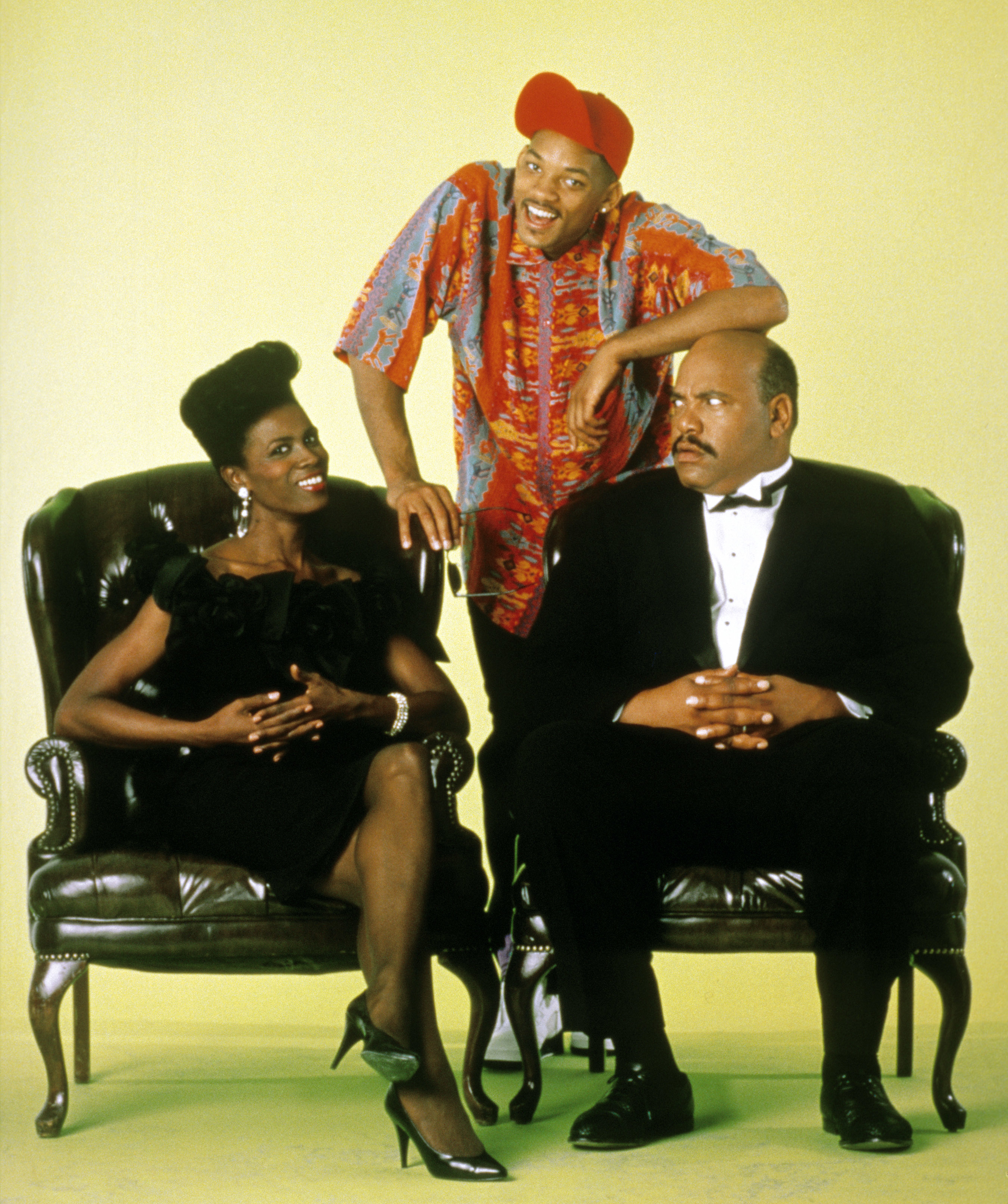 Three characters from &quot;The Fresh Prince of Bel-Air&quot; in a promotional photo, posing humorously with one standing, one seated, and one leaning