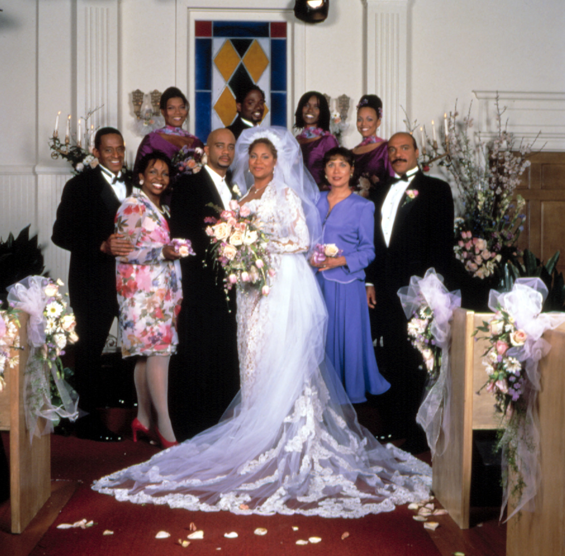 Group wedding photo with bride in a long gown, groom, and guests in formal attire standing in a church