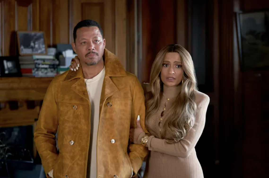 Terrence Howard and an unidentified woman stand together, he in a suede jacket, she in a knit dress