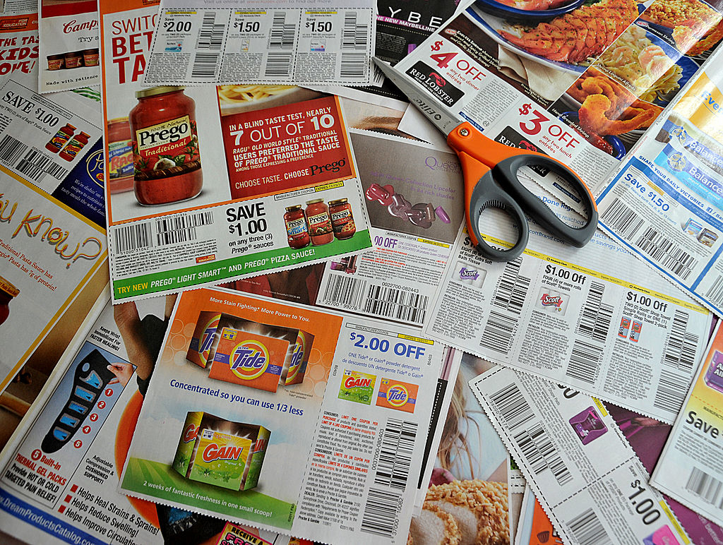 Assorted clipped coupons spread out next to scissors on a table, promoting various products and discounts