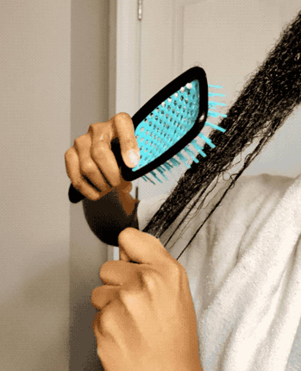 Person brushing wet hair with a blue-toothed comb, wearing a white bathrobe