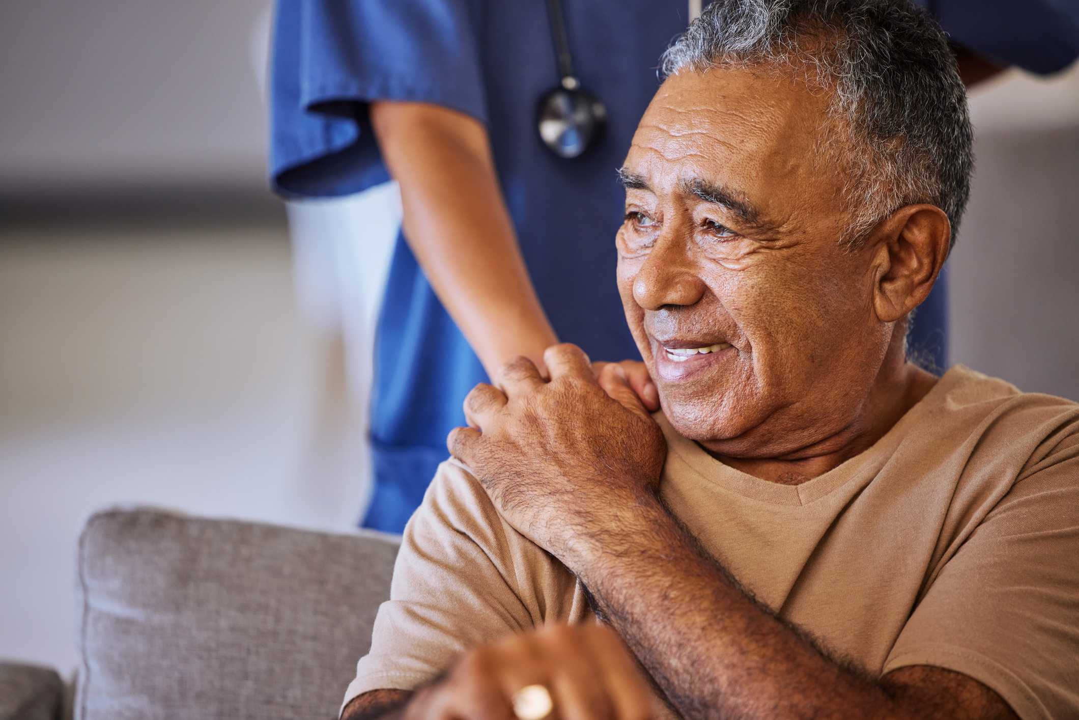 Smiling elderly man at home with a nurse placing a hand on his shoulder, displaying care