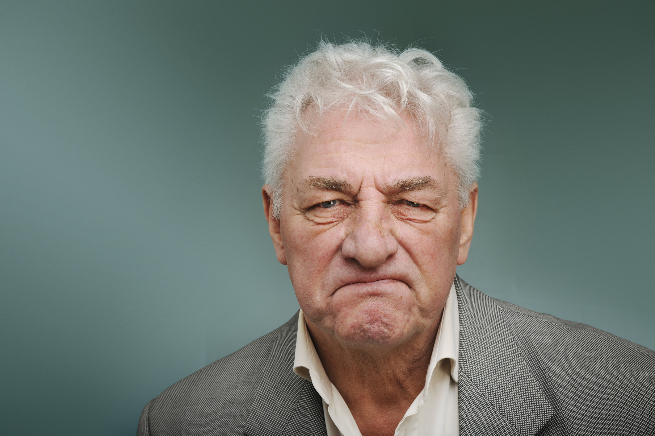 Older man with a discontent expression wearing a white shirt and gray jacket