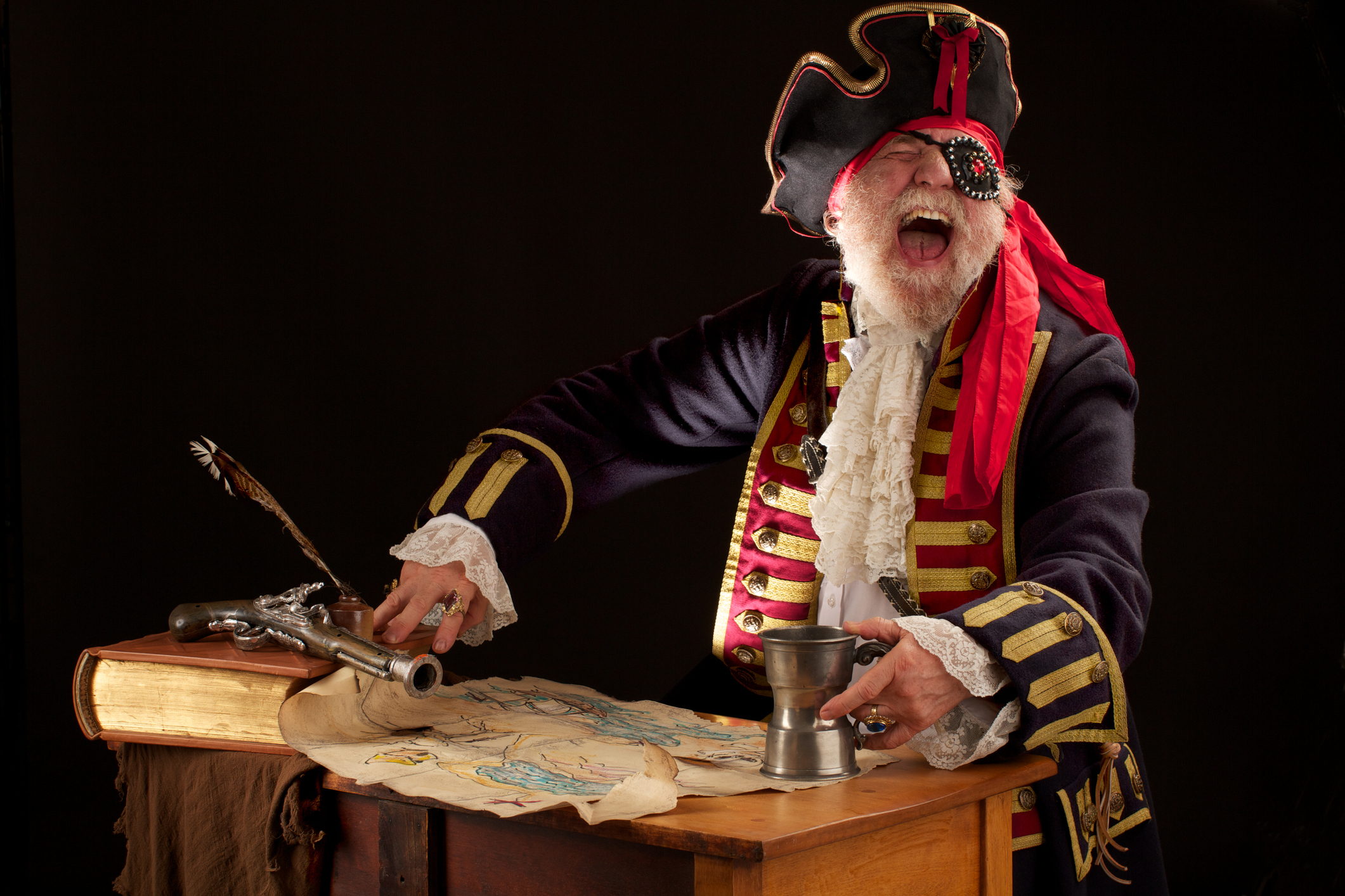Person dressed as a pirate with a feathered hat, gesturing dramatically at a desk with a map, quill, and pistol