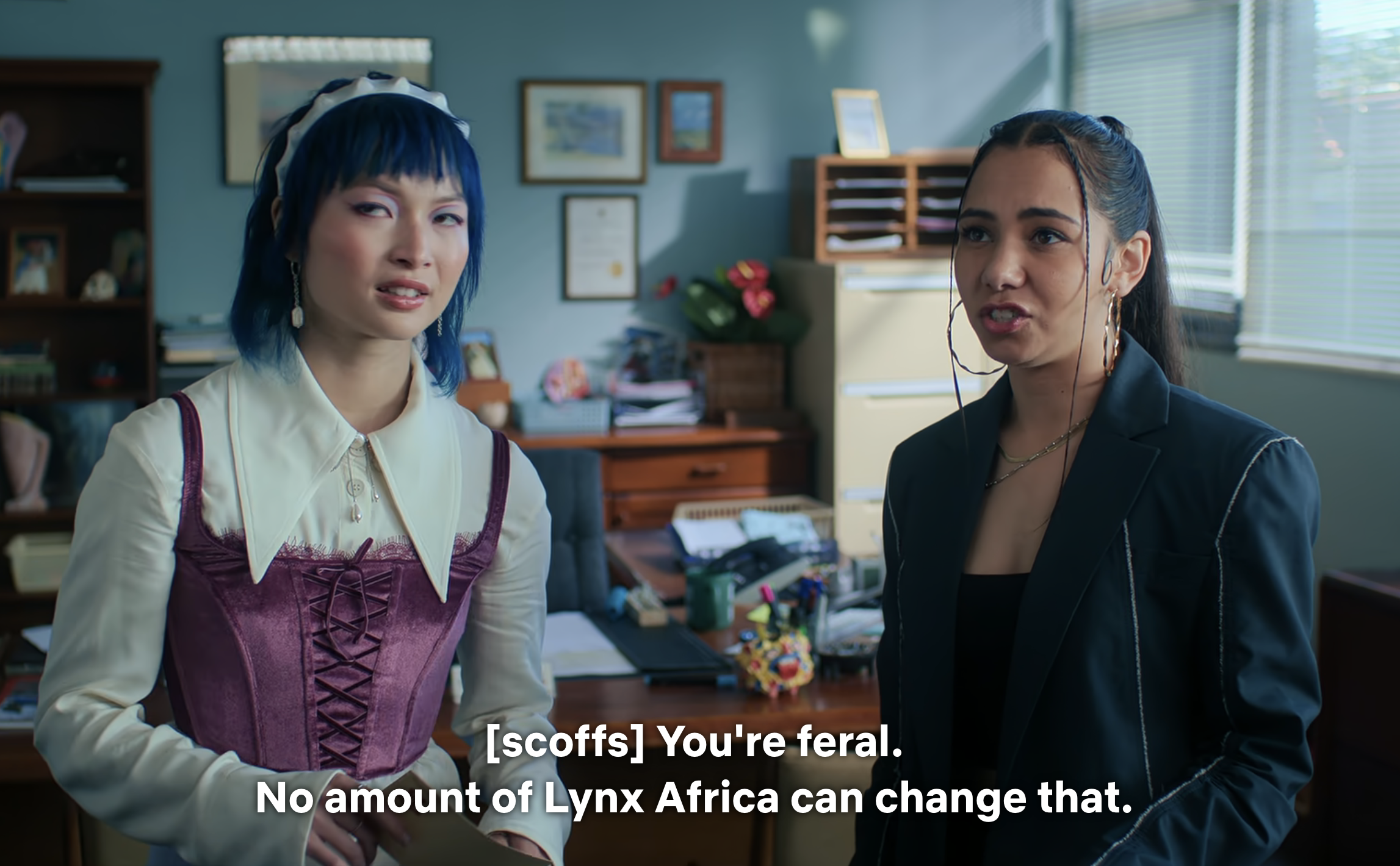 Two characters from a TV show in a scene, one in a vest and blouse, the other in a blazer, with dialogue subtitles