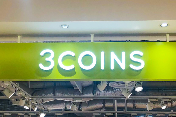 店舗の看板に「3COINS」と書かれている。店内は照明で明るく照らされている。