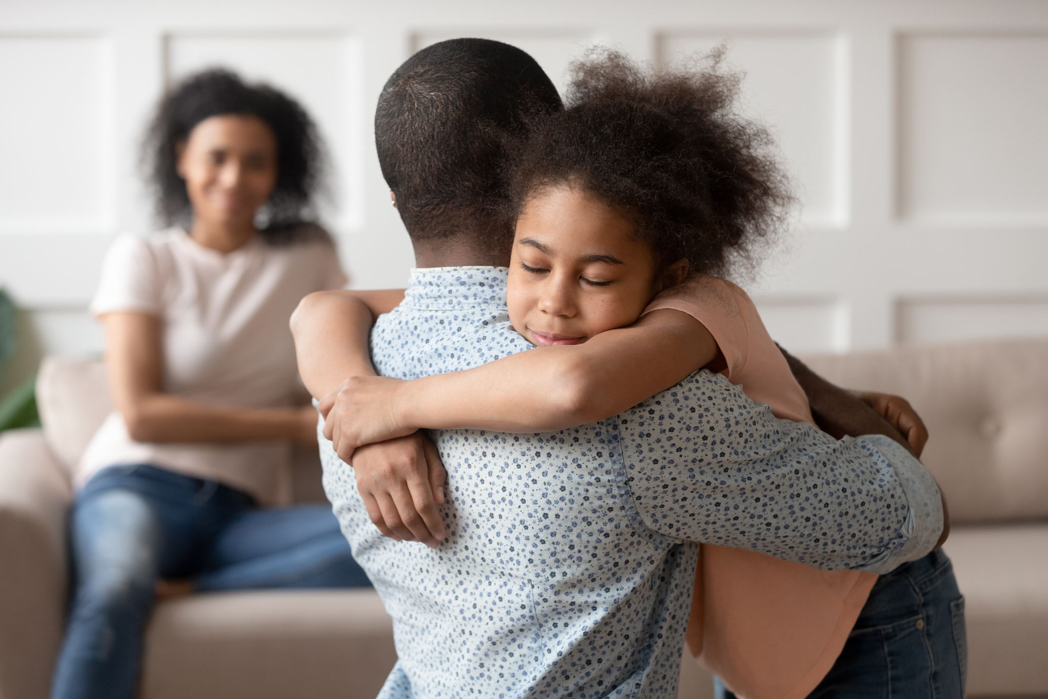 Man embracing young girl, woman smiling in background, family moment at home