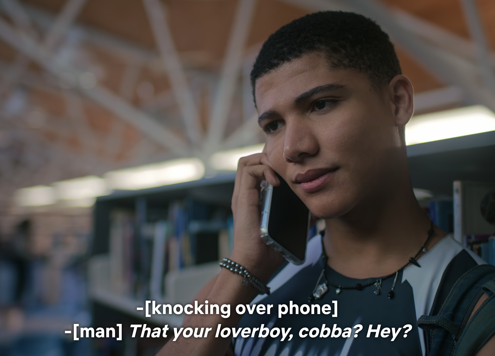 Miguel from Cobra Kai on a phone call in a school hallway; subtitles depict mocking dialogue