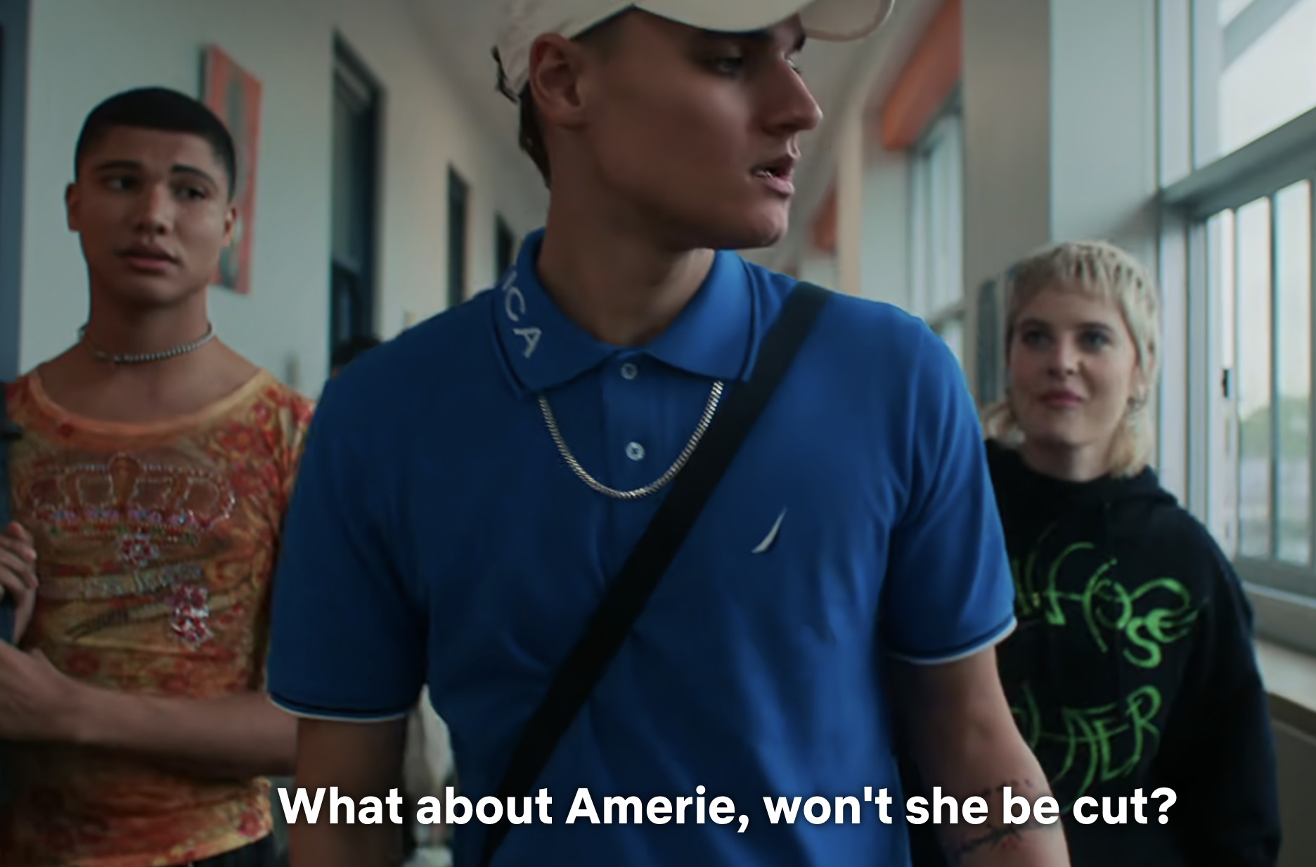 Three actors on set, one in foreground wearing a cap, subtitled scene from a TV show