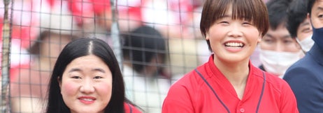 広島カープのユニフォームを着た2人の女性が野球場で笑顔で立っている。