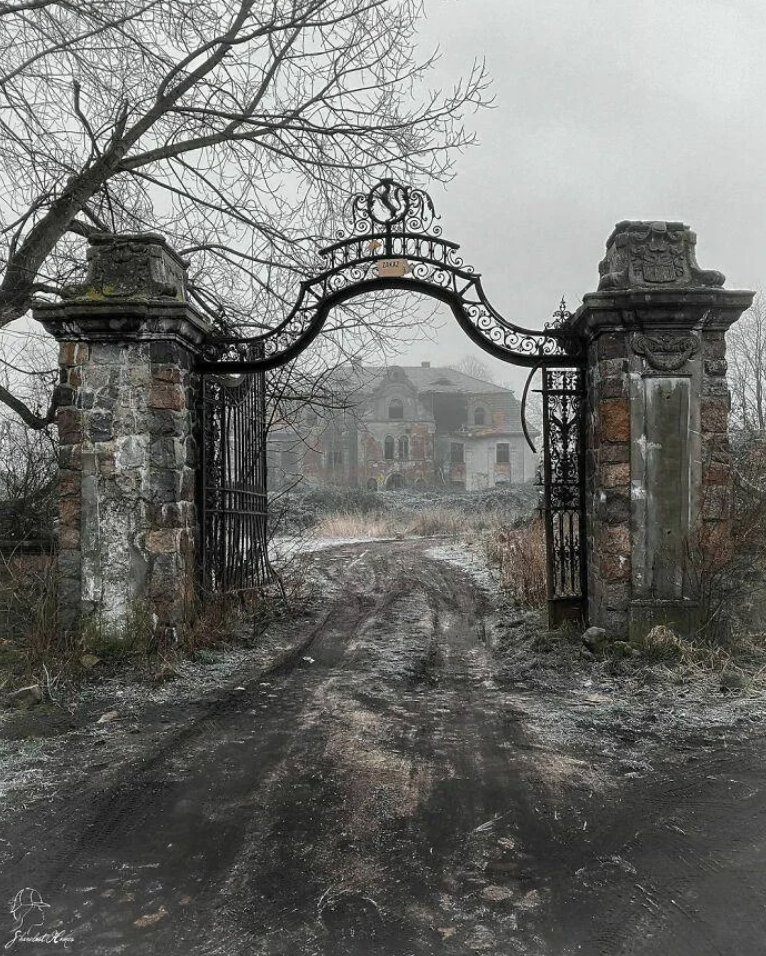 Worn iron gate opens to a dilapidated mansion with bare trees, evoking a mysterious, eerie atmosphere
