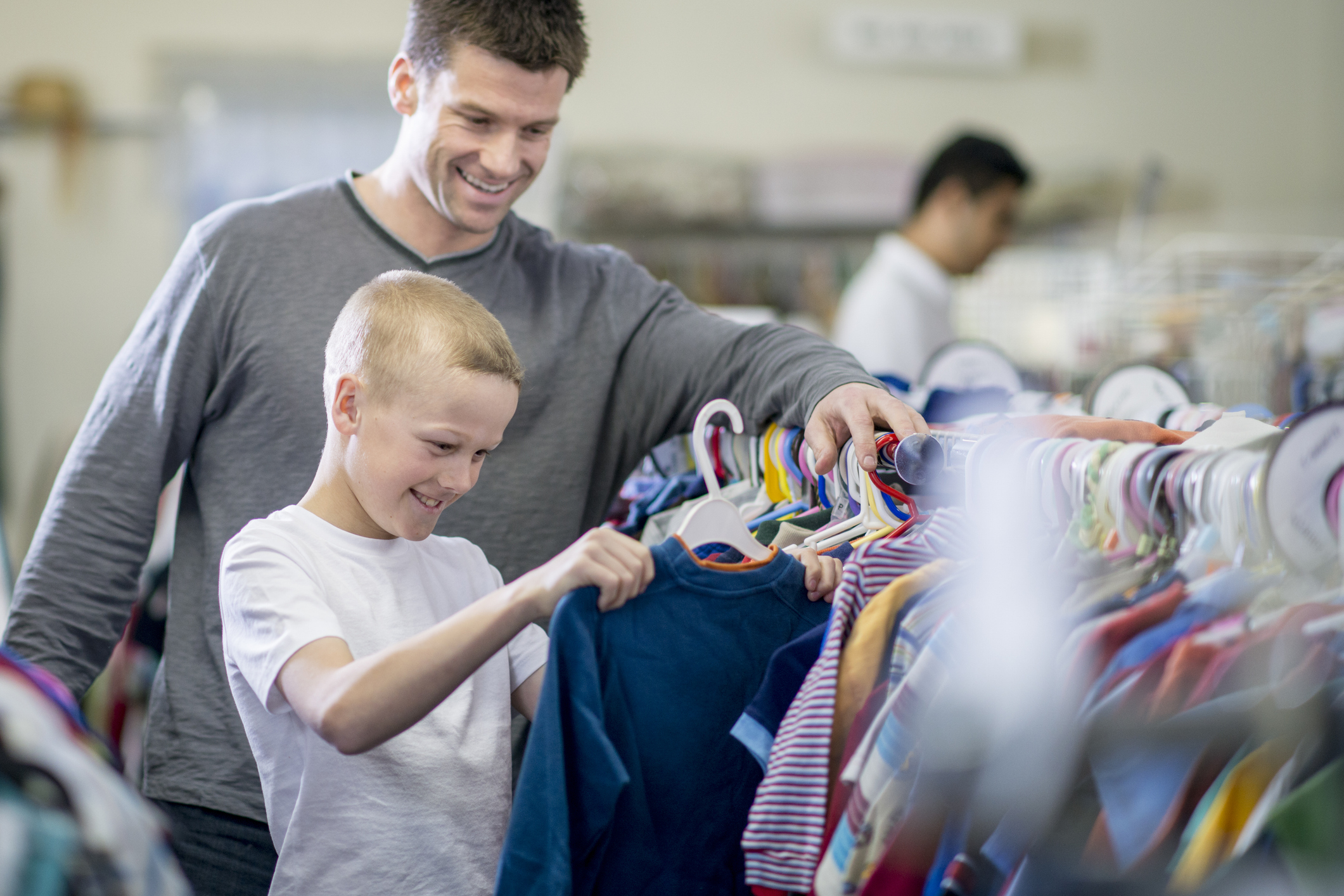 Adult and child smiling, selecting clothes from a rack in a thrift store setting