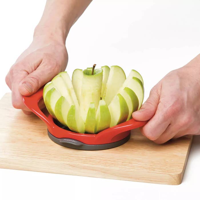 A person using an apple slicer to cut an apple on a wooden board