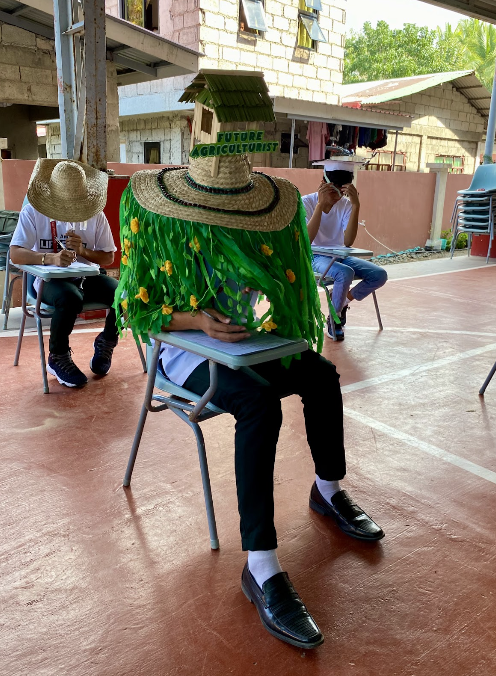 Person seated wearing a large hat with &quot;Future Agriculturist&quot; text