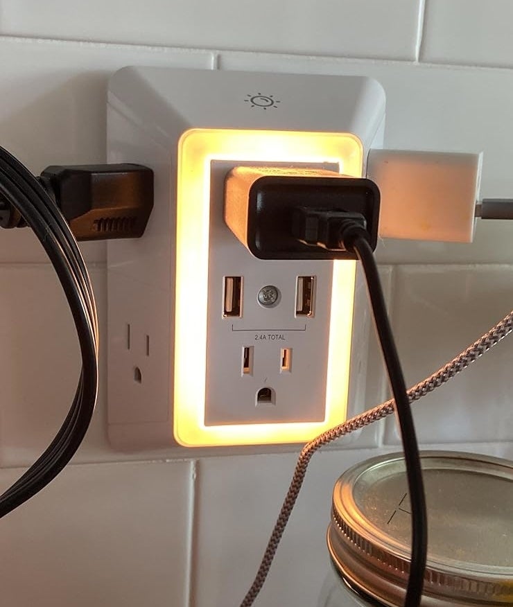 Outlet with USB ports and a nightlight feature, two cords plugged in, adjacent to kitchen tiles