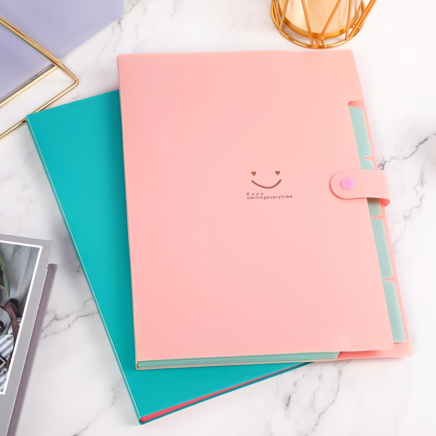 Two pastel binders with a smiling face design, one with a strap closure, on a marble surface